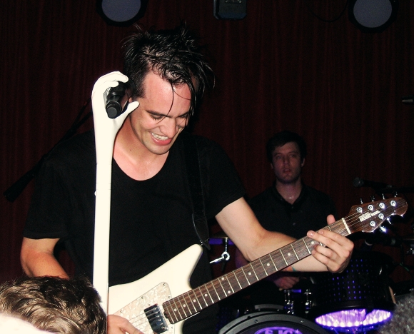 Brendon Urie smiling as he rocks it out on the guitar.